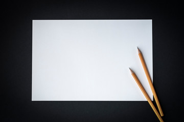 a white sheet of paper and pencils in a frame of black background