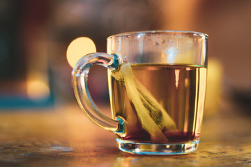 A glass cup containing green tea as the tea bag sits stationary inside.
