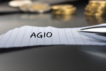 Agio auf einem Zettel mit Stift vor Geldmünzen