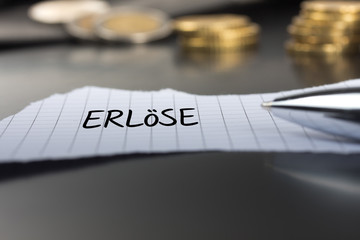 Erlöse auf einem Zettel mit Stift vor Geldmünzen