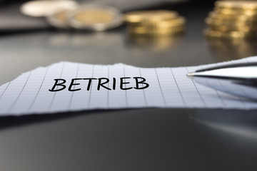 Betrieb auf einem Zettel mit Stift vor Geldmünzen