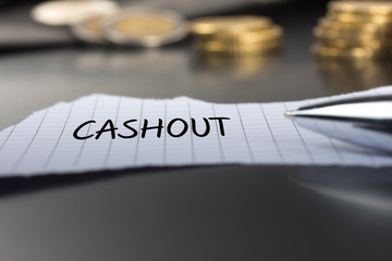 Cashout auf einem Zettel mit Stift vor Geldmünzen