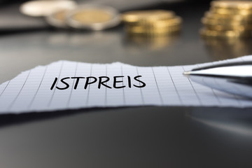 Istpreis auf einem Zettel mit Stift vor Geldmünzen