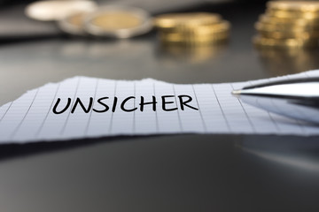Unsicher auf einem Zettel mit Stift vor Geldmünzen