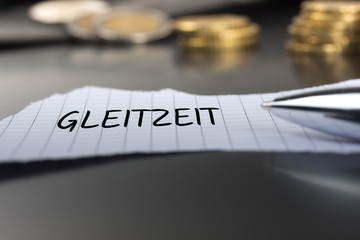 Gleitzeit auf einem Zettel mit Stift vor Geldmünzen