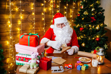 Fototapeta na wymiar Merry Christmas and Happy Holidays. Santa Clause is preparing gifts for children for Xmas at desk at home.