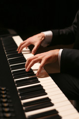Naklejka na ściany i meble Hands on piano. The pianist plays the piano. Piano keys on black background