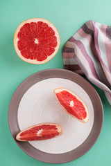 Two grapefruit slices on a plate, striped napkin against turquoise table. Minimal style trendy pastel colors. Healthy lifestyle.