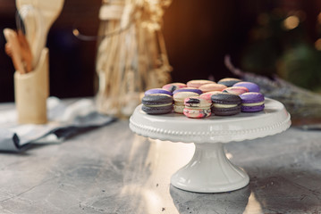Colored macarons on a white tray on a marble table with a napkin and kitchen accessories on the background.