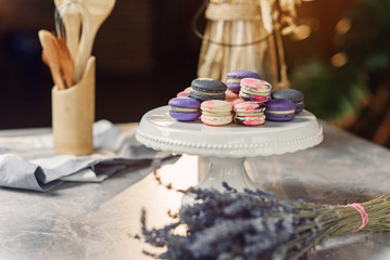 Colored macarons on a white tray on a marble table with a napkin, lavender and kitchen accessories.