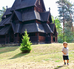Little two years old boy running and playing in front of the Gol Church,  a stave church originally built in Gol city, but now located in the Norwegian Museum of Cultural History at Bygdoy in Oslo, No © nachosuko