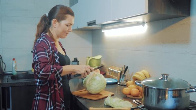 woman in the kitchen preparing a meal concept. girl in the kitchen cuts cabbage with a knife. cook vegetarian food healthy food. girl at home in the kitchen slow lifestyle motion video