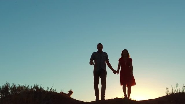 couple silhouette walking holding hand toward the sun outdoors at sunset dramatic sky background. young happy couple go on nature sunset sun light. man and girl silhouette love friendship at sunset