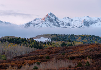 Snow capped peaks rise to meet pastel sunset colored skies in the Colorado Rockies