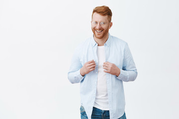 Sure he will get what want. Portrait of confident and happy handsome redhead guy with bristle, touching shirt with self-assured and uplifted expression, smiling broadly, getting ready to go out