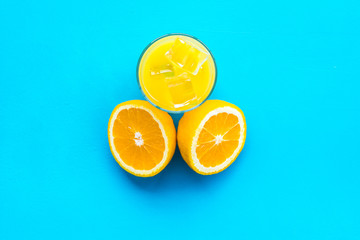 Glass of cold orange juice near halfs of fresh oranges on blue background top view copy space