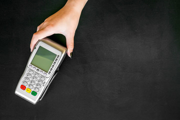 Offer a payment terminal. Woman's hand hold POS terminal on black background top view space for text