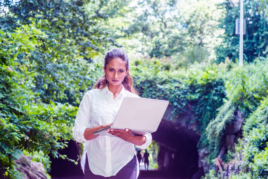 Young East Indian American Woman Traveling, Working In New York, Holding Laptop Computer, Walking At Central Park, Looking. Street Bridge With Leaves On Background. Color Proton Purple Filtered Look..