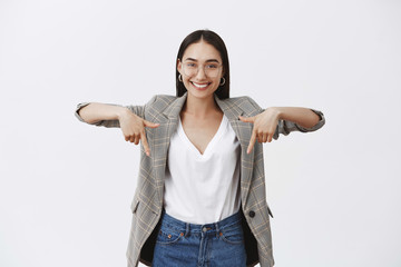 You should check it out. Portrait of charming happy young entrepreneur in eyewear and stylish jacket, pointing down with raised hands and smiling with self-assured satisfied expression © Cookie Studio