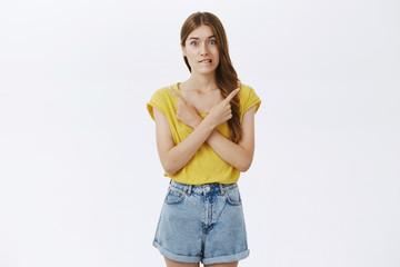 Hesitant girl worries to make choice pointing right and left in different corners of copy space...