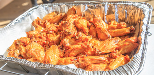 Fried Naked Chicken Wings: Fried naked chicken wings in a foil tray just after being cooked.
