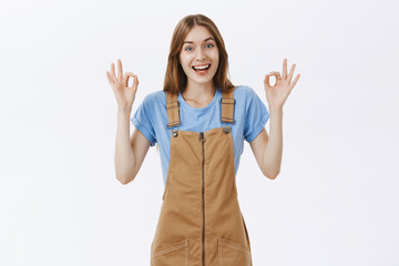 Everything okay, chill. Friendly and enthusiastic good-looking female in brown overalls showing ok...