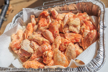 Raw Seasoned Chicken Drummettes and Flats:  Raw seasoned chicken drummettes and flats in a foil tray prepared for cooking.