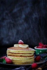 Stack of homemade fluffy pancakes on dark moody background