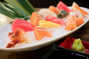 Mixed sliced fish sashimi on ice in white bowl. Sashimi Salmon Tuna Hamachi Prawn and Surf Calm set, raw fish, japanese food in Asian restuarant.