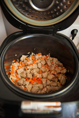 Raw meat in the slow cooker. Carrots and onions. The beginning of preparations.