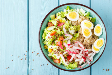 Bowl with wheat porridge, boiled quail eggs and fresh vegetable salad of radish, corn, sweet pepper and chinese cabbage. Healthy and delicious dietary lunch. Vegetarian, vegan food. Top view. Flat lay