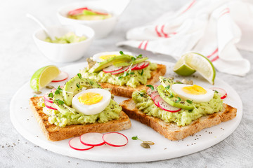 Fototapeta na wymiar Toasts with avocado guacamole, fresh radish, boiled egg, chia and pumpkin seeds. Diet breakfast. Delicious and healthy plant-based food. Flat lay. Top view