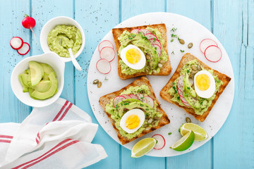 Toasts with avocado guacamole, fresh radish, boiled egg, chia and pumpkin seeds. Diet breakfast. Delicious and healthy plant-based food. Flat lay. Top view