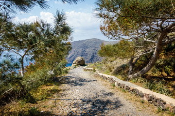 Fototapeta premium Dirt road leading towards rocky cliff and Santorini island; Greece