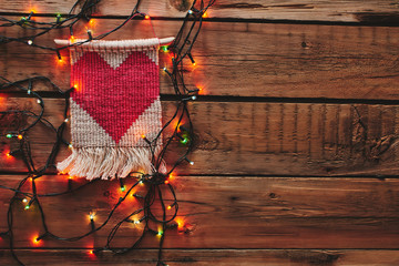 Macrame with a red heart framed by a Christmas garland on a wooden table. A gift for Valentine's Day.