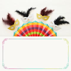 carnival party celebration concept with masks and colorful fan over white wooden background. Top view.