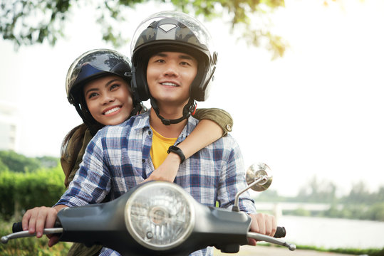 Smiling Young Vietnamese Couple In Helmets Riding On Bike Together