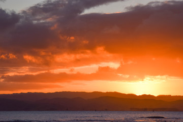 A coral colored sky while the sun sets above the beach in Gisborne, New Zealand.