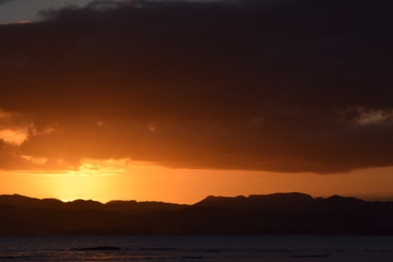 A dark hill l;andscape below the sinking orange sunset at Gisborne, New Zealand.
