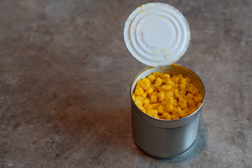 Canned corn in open aluminum can on  grunge gray table with copy space for text. Canned vegetarian food.