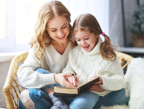 happy family mother reads book to child to daughter by window .