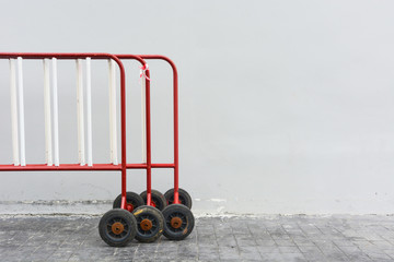 old red and white road security steel barrier on wheel, on grey cement wall background and pathway, copy space