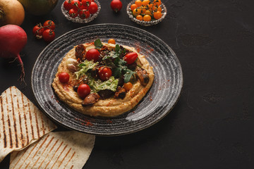 Hummus with vegetables and seafood on black background