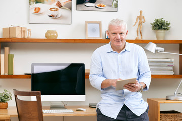 Portrait of positive mature It engineer with digital tablet standing at hie workplace