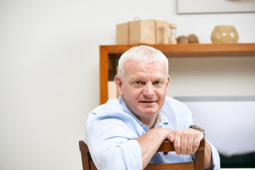 Fototapeta premium Portrait of middle-aged businessman sitting on chair in office and looking at camera