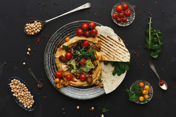 Hummus with vegetables and seafood on black background