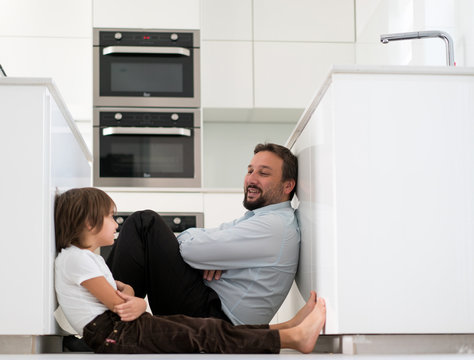 Father and son sitting on floor in kitchen and talking