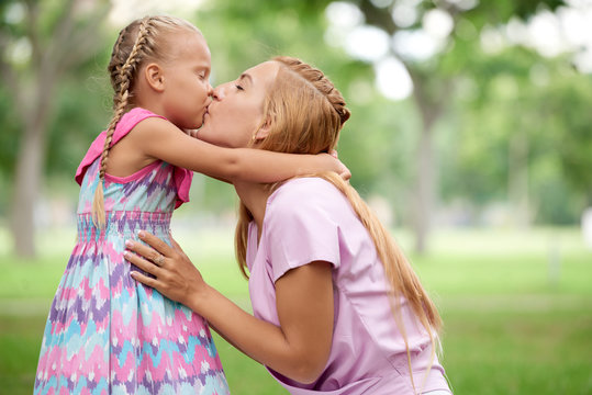 Happy young mother kissing her little daughter in bright suumer dress