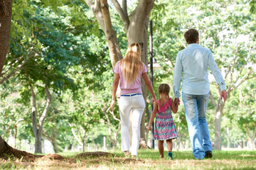 Fototapeta premium Rear view of mother and father holding hands of their daughter when walking in park