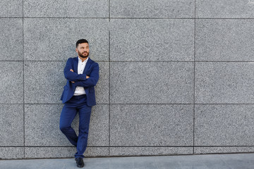 Handsome businessman posing near gray wall on street background